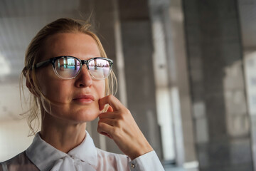 Close-up portrait of a beautiful blonde business girl, office worker or student in a white shirt and glasses, which reflect the office building, university