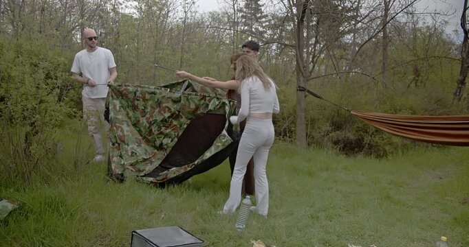 Two couples and friends collaborate to assemble a camping tent amidst a beautiful natural landscape. This scene captures the joy of an outdoor family getaway and the bond of friendship.