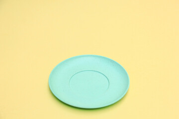 A simple blue plate on a bright yellow background, highlighting its clean, empty space and minimalist design
