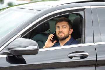 Man making a phone call while parked in a black car on a bright day