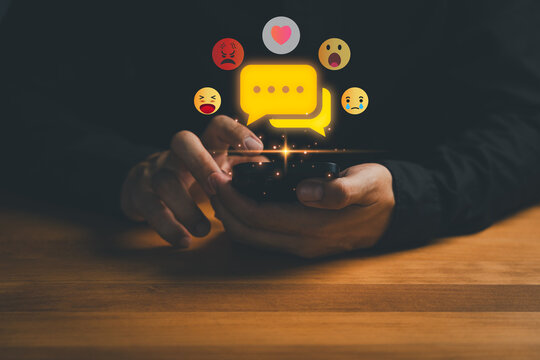 Close-up of hands using smartphone with chat bubble and emoji reactions. Concept of social media communication, online chat, messaging app, emotional expression, feedback and digital interaction.