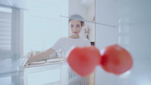 A young woman opens the fridge to find only two tomatoes inside. She takes them out and closes the door, capturing a quiet moment of simplicity and everyday life - Powered by Adobe