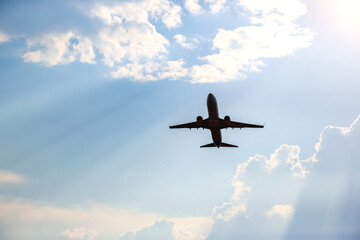 Airplane flying under bright sky with clouds during late afternoon