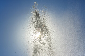 Water fountain sprays sunlight into a clear blue sky during a bright afternoon