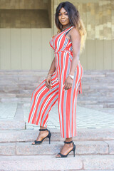 An African woman stands gracefully on steps, showcasing a stylish striped jumpsuit