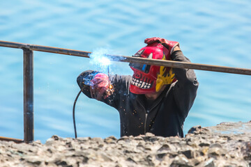 Welding activity on rocky coastline with ocean in background during bright sunny day