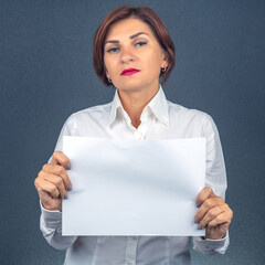 Woman in white shirt holding blank paper in studio setting with dark background