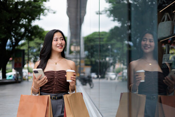 Young woman walking in the city, holding shopping bags and using her smartphone