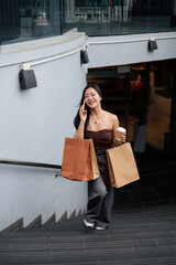 Happy customer walking down the stairs talking on the phone and holding shopping bags