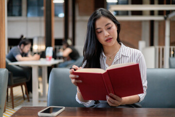 Fototapeta premium Young asian businesswoman reading a book in a modern coworking space