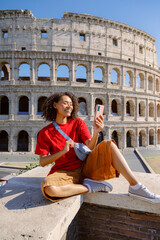 A cheerful young woman enthusiastically takes a vibrant selfie at the iconic Colosseum in Rome, fully enjoying her delightful travel experience while making beautiful memories along the way