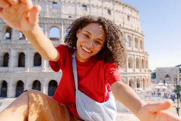A joyful young woman poses with arms outstretched in front of the historic Colosseum in Rome, embodying the essence of travel, adventure, and happiness during her city exploration