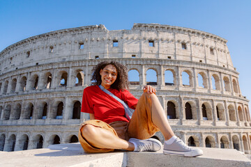A cheerful, young woman happily poses in front of the iconic Colosseum in Rome, showcasing the magnificent beauty of Italian architecture and the vibrant atmosphere of tourism that surrounds it