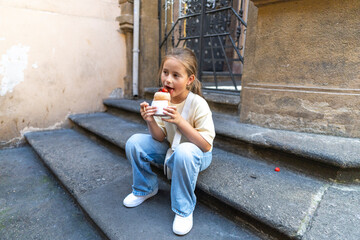 A cheerful child sits on warm stone steps, enjoying a delicious dessert in a vibrant urban setting. This scene captures the joy and simplicity of childhood experiences that bring delight to life