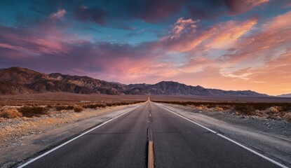 Empty road stretching into a vibrant sunset over mountains