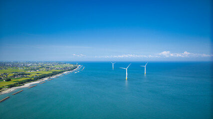 残暑の中の日本の富山県東部の海岸線で発電をしている洋上風力発電風車の様子 © crossover.japan