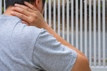Asian man massages sore neck after workout, relieving muscle tension and cervical strain. Outdoor...
