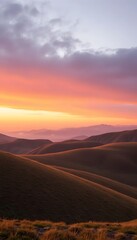 Fototapeta premium Vibrant sunset sky illuminates rolling hills and distant mountains in a serene landscape