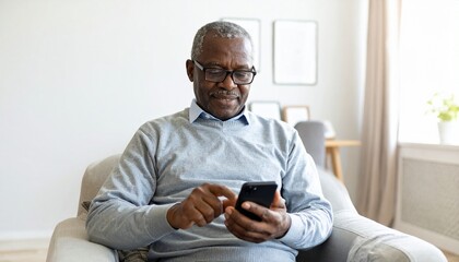 Senior African American man using a smartphone while sitting in an armchair at home.