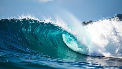 Obraz premium A powerful, turquoise ocean wave curls and breaks under a clear blue sky, creating a spectacular display of nature's force