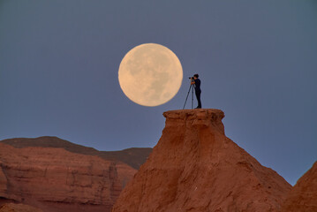 A photographer captures the full moon over a serene desert at dusk