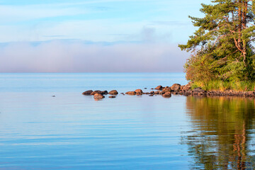 Summer morning landscape of a large lake, a veil of fog over the horizon.