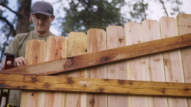 Worker Leveling Cedar Fence Board During Construction