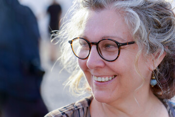 Close-up of cheerful mature woman with eyeglasses, enjoying golden hour sunlight, showcasing a...