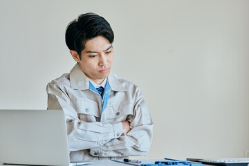 腕を組んで考える作業服姿の日本人男性
