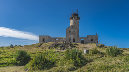 An old lighthouse on a tropical island. A dilapidated building with empty window openings and a...