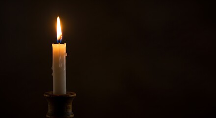 A single white candle burning brightly on a dark background with wax drips and a small candle holder base