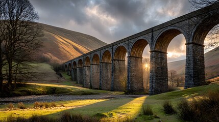 A magnificent stone viaduct stretches across a valley bathed in golden sunlight, highlighting the architectural grandeur and natural beauty of the landscape.