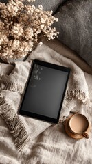 Tablet, coffee, and dried flowers on a linen blanket