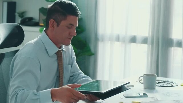Professional engineer looking at phone while working on tablet with green screen at meeting table with turbine engine or jet engine sketch design and various metal gear scatter around. Alimentation.