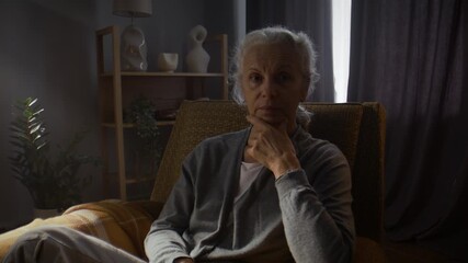 Pensive senior woman sits thoughtfully in armchair in living room - Powered by Adobe