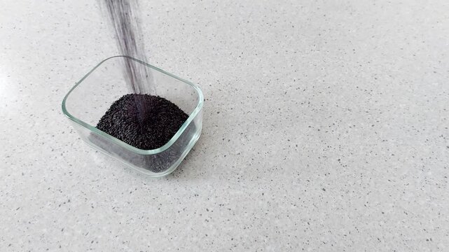 Black poppy grains drift gently into clear glass-each speck a quiet echo of time, falling in slow motion like ash on still water. A minimalist study in texture and gravity
