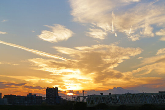 Vivid sunset over city skyline with dramatic golden clouds and bridge silhouette. Warm evening light contrasts with the cool blue sky.