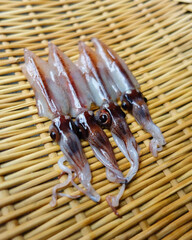 Fresh squid aligned neatly on woven basket.
