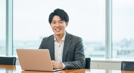 若手男性社員がパソコンの前で笑顔を浮かべているポートレート	