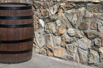 Empty oak barrel stands against a stone wall, illuminated by the sun. Wine barrel with a black...