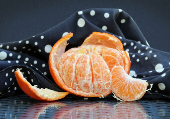 Still life with peeled tangerine and black and white polka dot napkin on glass top table. Dark background. Selective soft focus.