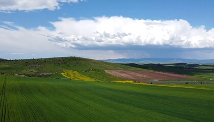Obraz premium Rolling hills with vibrant green fields under a partly cloudy sky