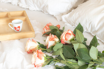Enchanted Morning in the bedroom with bouquet of roses on a soft bed with a tray featuring a coffee cup. Love, Valentine’s Day, romance.