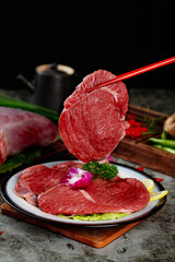 Fresh Raw Beef Steak Cut Held with Chopsticks Above Plate of Sliced Meat on Wooden Board