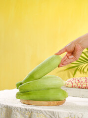 Fresh Sweet Corn Cobs with Green Husks on Wooden Board Against Yellow Background