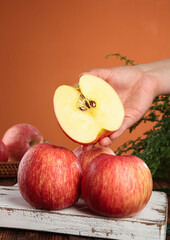 Fresh Red Striped Fuji Apples with Hand Holding Cut Apple Half on Rustic Wood Surface