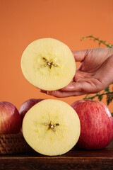 Fresh Luochuan Fuji Apples - Hand Holding Sliced Red Striped Apple Half on Orange Background