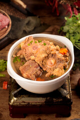 Spicy Beef Tailbone Stew with Vegetables in Traditional White Bowl on Rustic Wooden Table
