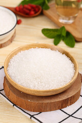 White granulated sugar in wooden bowl on kitchen table with fresh herbs and cooking ingredients