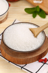 White granulated sugar in glass bowl with wooden spoon on cutting board
